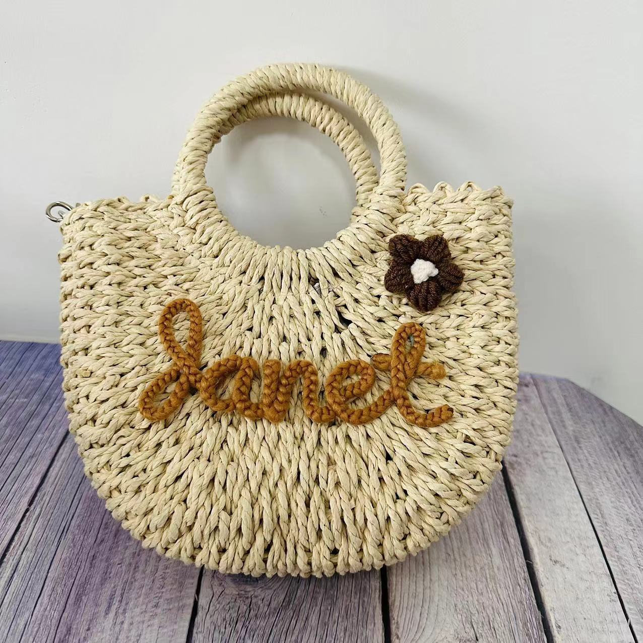 Straw tote bag with personalized letter design, seaside vacation style, featuring a woven flower accent.