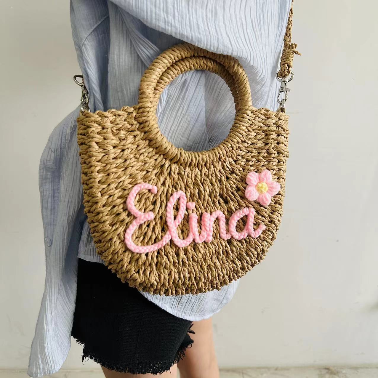 Grass woven straw tote crossbody bag with pink name "Elina" and floral decoration, showcasing seaside vacation style.