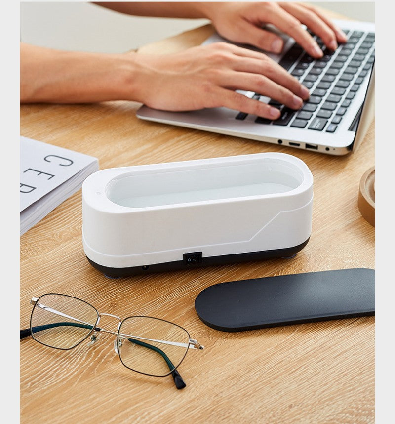 Ultrasonic eyeglasses cleaner in white, multifunctional tool on desk, alongside eyeglasses and laptop.