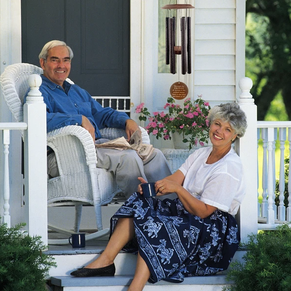 Two smiling people sitting on a porch with a 34-inch memorial wind chime, bronze color, hangs nearby.