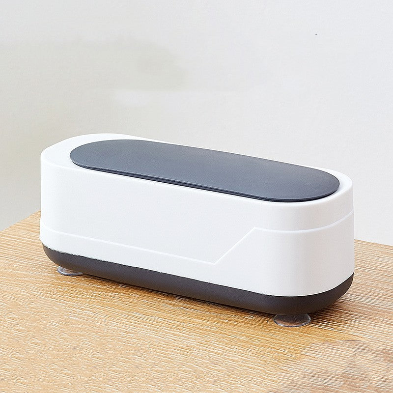 Ultrasonic eyeglasses cleaner in white with black accents on a wooden surface.